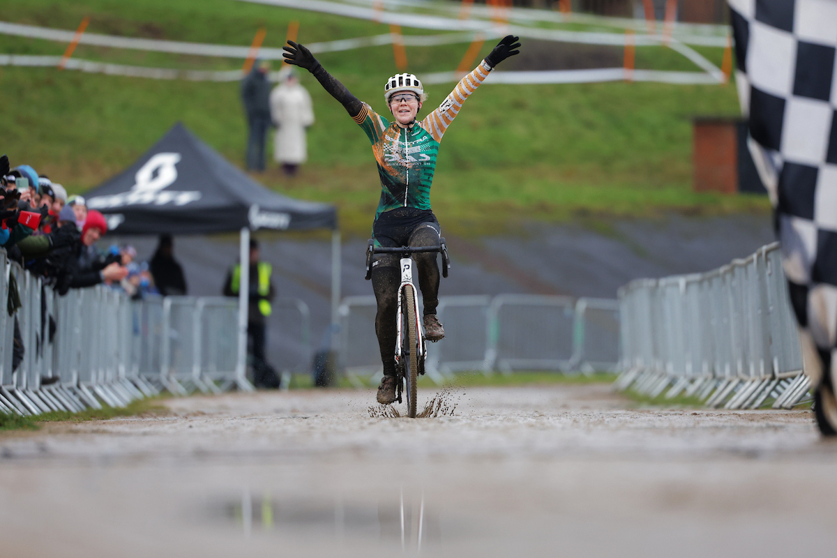 Woman crosses finish line on a bike with arms in the air