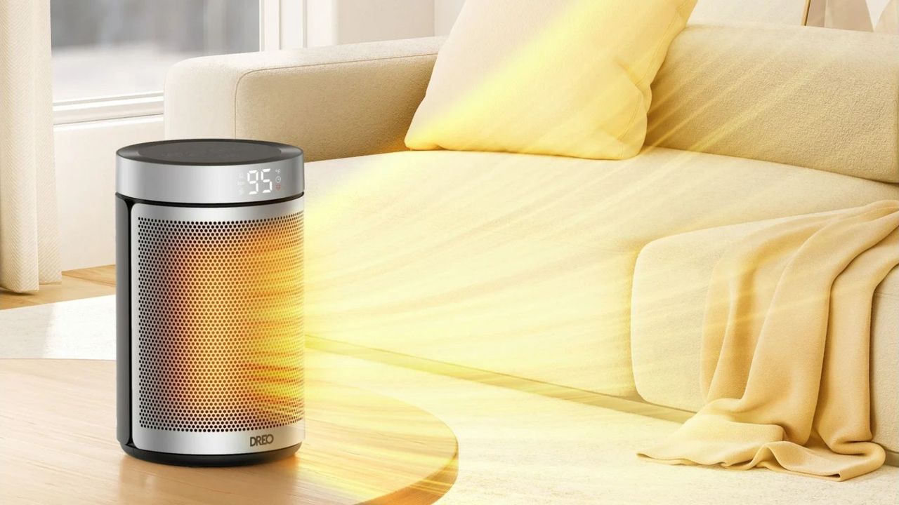 Dreo Portable 1500W Fast Ceramic Space Heater on coffee table with orange rays coming out representing heat, against beige sofa in living room