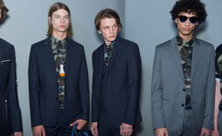 Three male models wearing dark coloured suites and patterned shirts by Dior Homme.