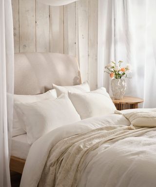 close up of bed in neutral and white shades with voile canopy and layers of cream bedding