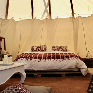 Inside of a luxury camping tipi with white bed and brown carpet