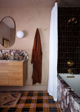 Bathroom with pink Roman clay walls, red and burgundy patterned floor, wood vanity unit with countertop and bath in burgundy-veined marble