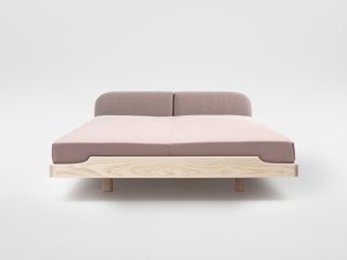 A minimalist wooden bed with low headboard upholstered in purple textile. The mattress is also covered in the same purple textile