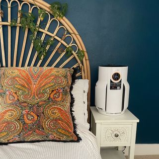 Shark NeverChange 5 Air Purifier sitting on a bedside table, next to a bed with striped white bedding and a wicker bedframe