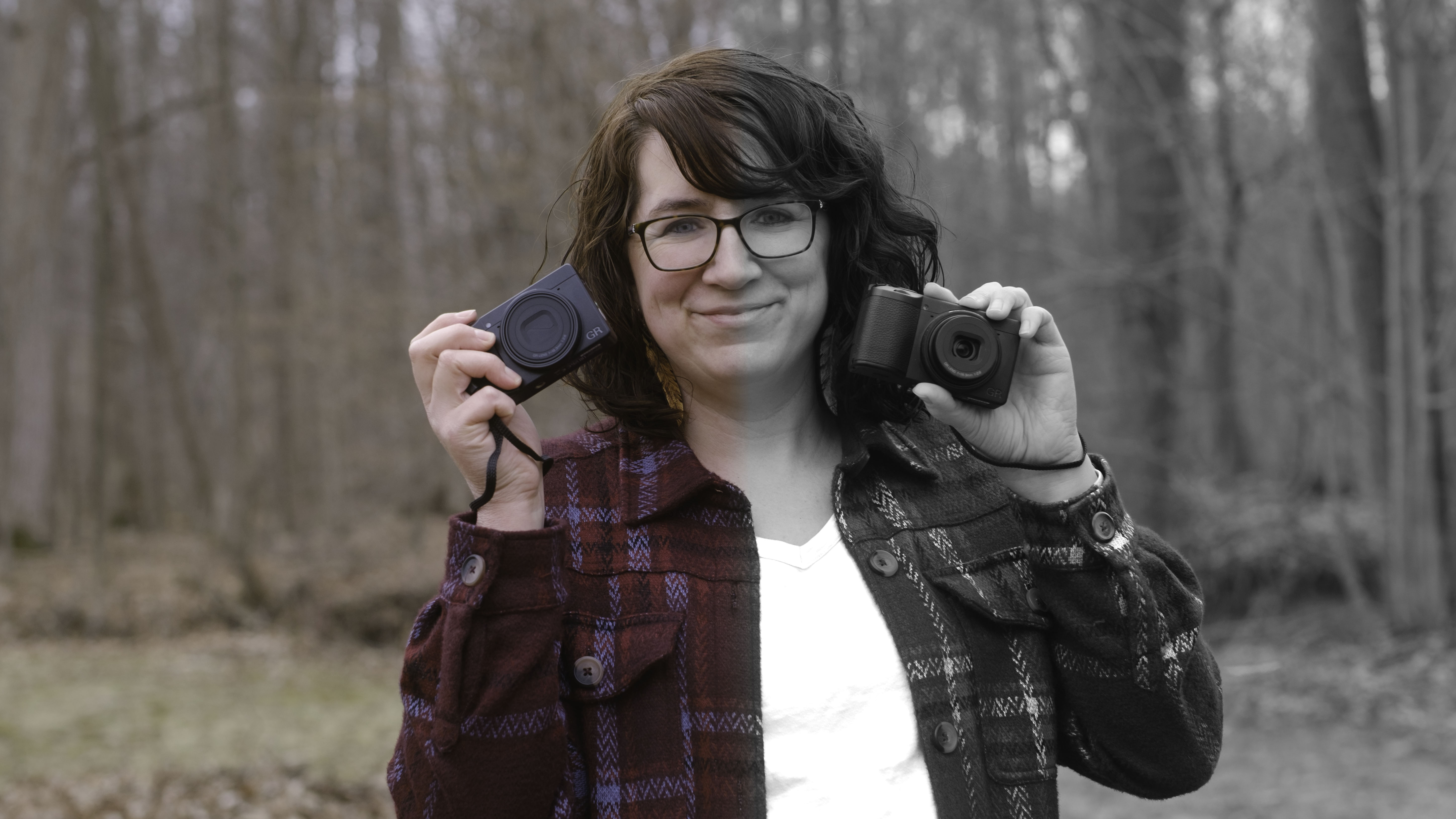 A photographer holds the Ricoh GR IV HDF in one hand and the Ricoh GR IV Monochrome in the other