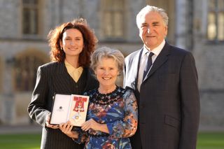 Bessie Carter, Imelda Staunton and Jim Carter posing outside Windsor Castle as Staunton holds up her Dame Commander of the British Empire