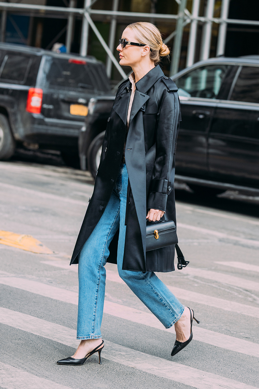A woman wearing a leather trench coat, blue jeans, and pointed toe heels