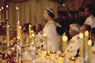 Queen Elizabeth standing up and speaking at a table filled with lit candles and guests