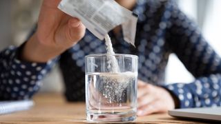 person pouring powder sachet into glass of water