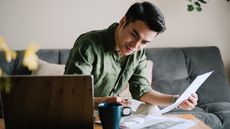 A young man works on financial planning on the sofa in his living room.
