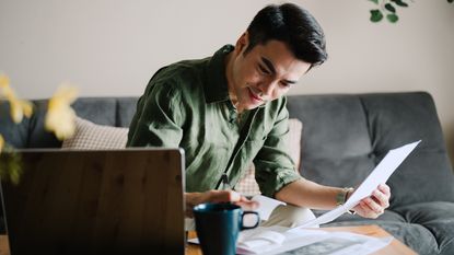A young man works on financial planning on the sofa in his living room.