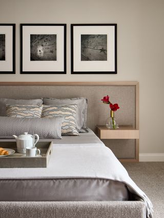 A bedroom with framed art above the bed, throw pillows on the bed and a vase of flowers on the nightstand