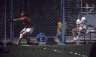 A vintage film photo of a man in red doing the hammer throw on a field