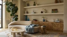 modern eclectic living space with neutral walls, long open styled shelving above a long burl wood vintage low console table with a curved couch and low stone coffee table