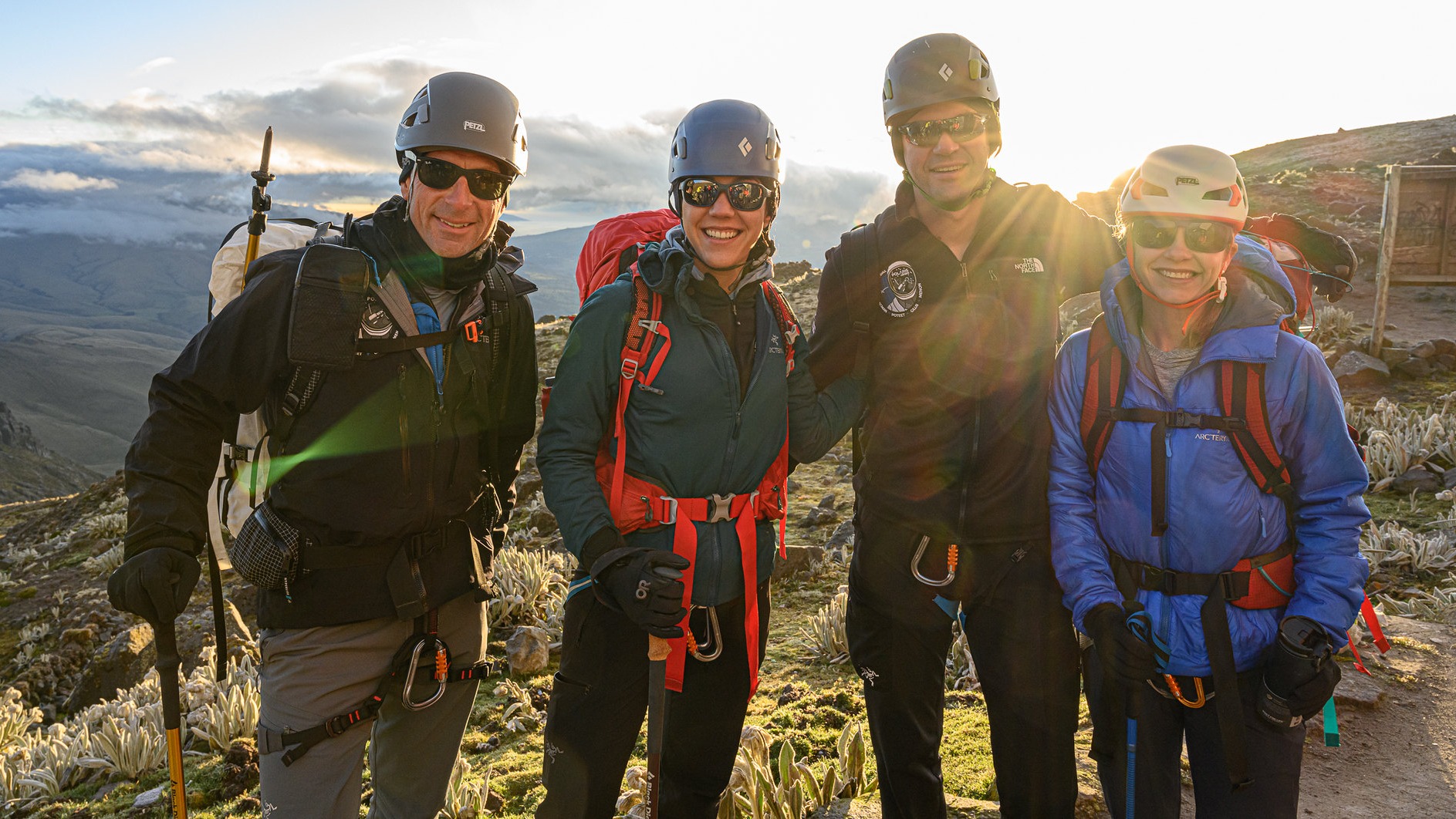 four astronauts hiking in the mountains with the sun shining behind