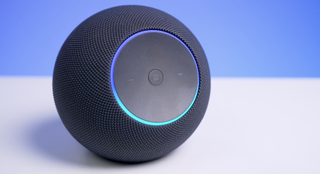 Echo Studio (2nd gen, 2025) on a white table with a blue background and the Alexa blue ring illuminated