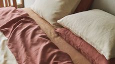 A close up of a bed with organic bedding in beige, muted red and orange tones