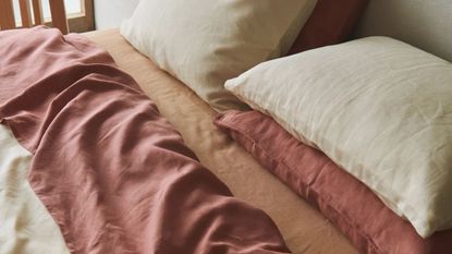 A close up of a bed with organic bedding in beige, muted red and orange tones