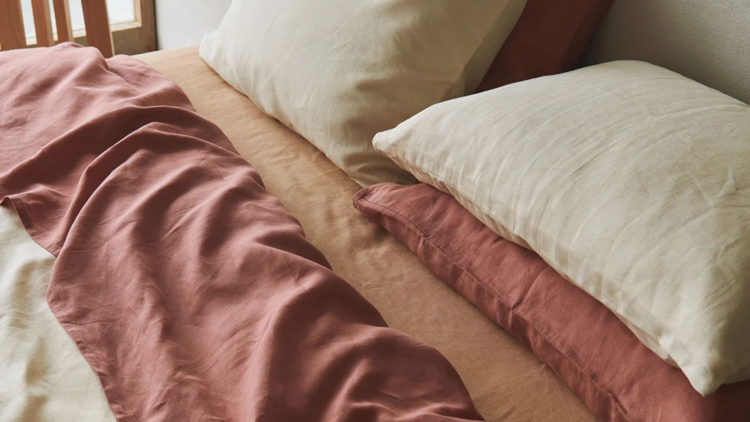 A close up of a bed with organic bedding in beige, muted red and orange tones