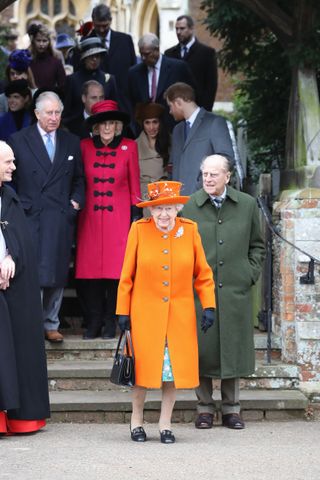 Queen Elizabeth wearing an orange coat and hat and Prince Philip wearing a green coat