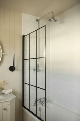 A modern bathroom with wood panelled walls, white subway tiled shower, and a black window frame effect bath screen