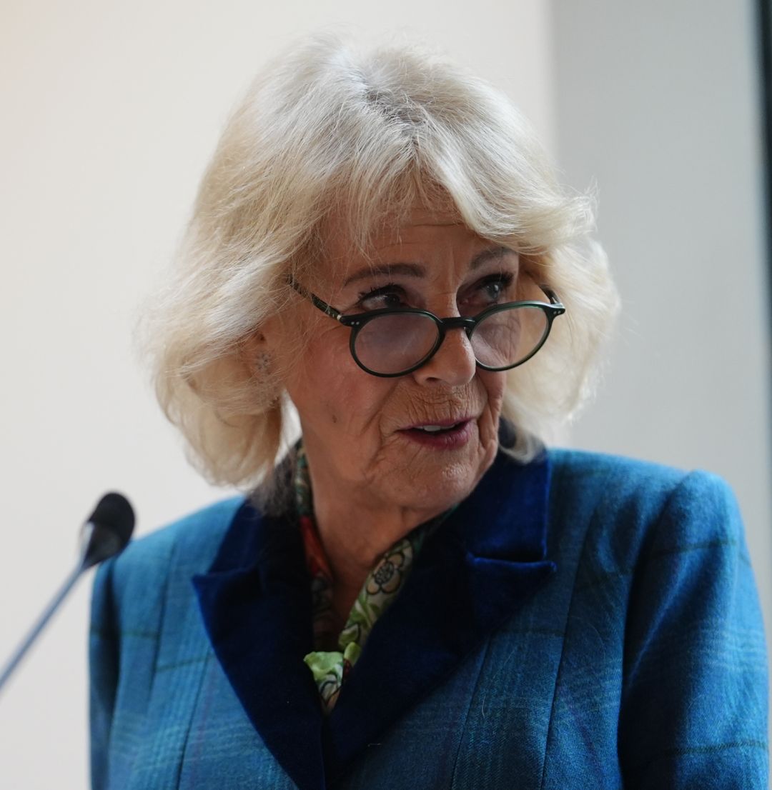 Queen Camilla speaking into a mic and wearing a blue suit