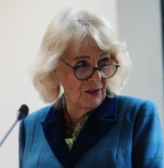 Queen Camilla speaking into a mic and wearing a blue suit