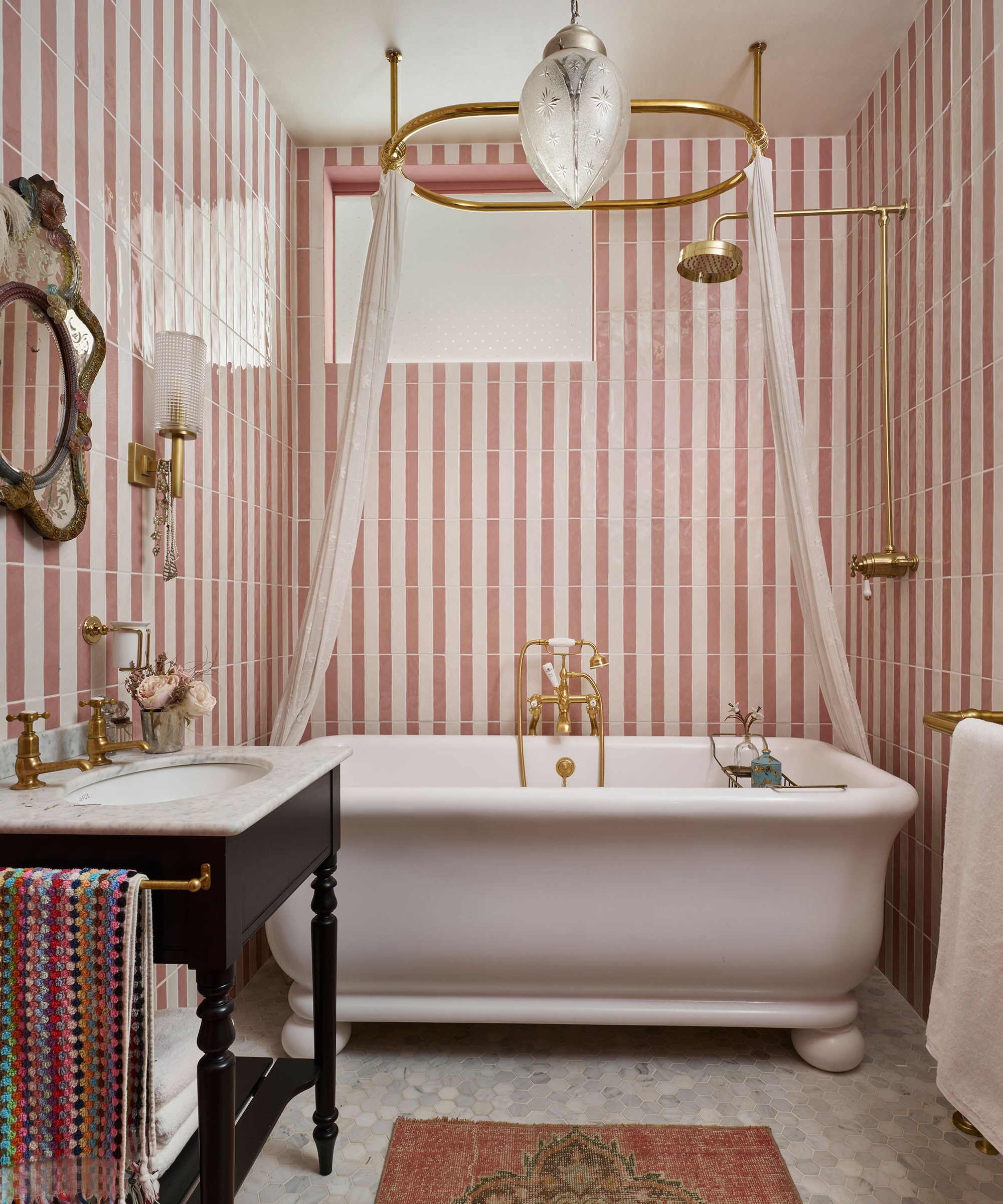 small bathroom with high level window and pink and white striped wall tiles with freestanding bath