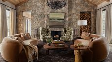 a stone clad mountain home with large glass windows, vaulted ceiling, fireplace, and two large velvet curved couches facing one another