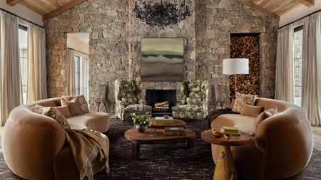 a stone clad mountain home with large glass windows, vaulted ceiling, fireplace, and two large velvet curved couches facing one another