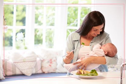 A woman holding a baby while eating from a plate