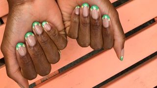 Daisy nail art on green French tips against orange background