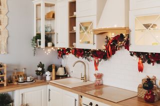 A modern, cream kitchen decorated for Christmas with a garland and some LED string lights.
