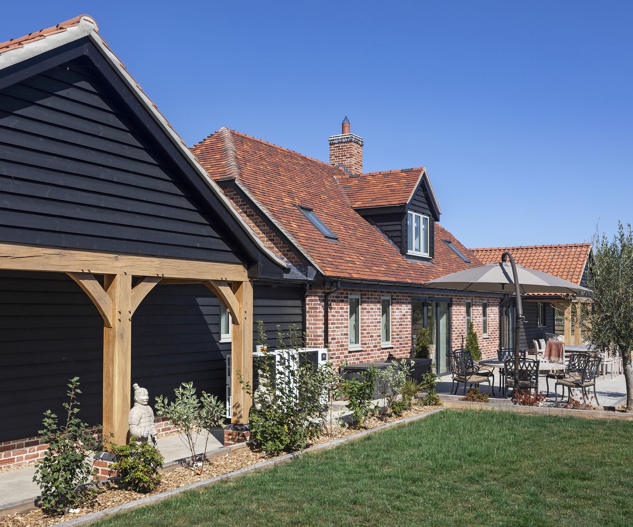A pitched roof, black timber clad oak frame extension next to a main home build from red brick