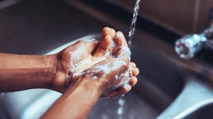 Cropped shot of an unrecognizable man washing his hands in the kitchen sink at home.