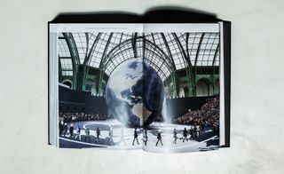 An open book with a photo of models walking in front of a large earth globe with a crowd of people on either side of the space.