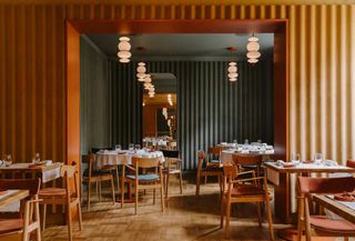 A restaurant interior featuring wooden floors, simple wooden chairs and circular lampshades hanging from the ceiling