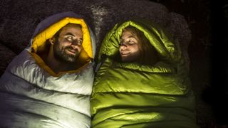 Man and a woman in sleeping bags lit by a lantern at night