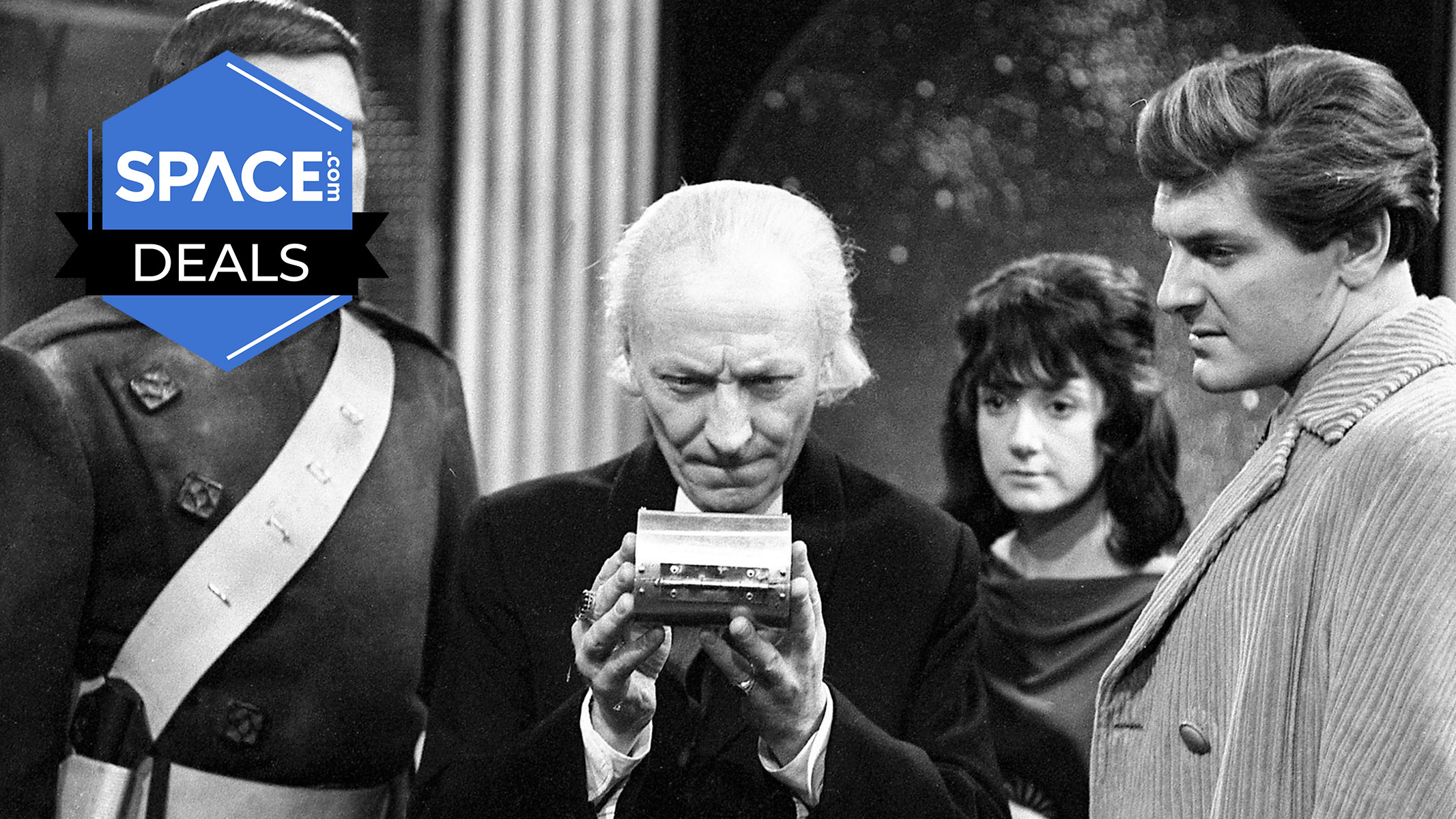 Four people are stood looking around an object as an elderly man in the center holds it, all in black and white.