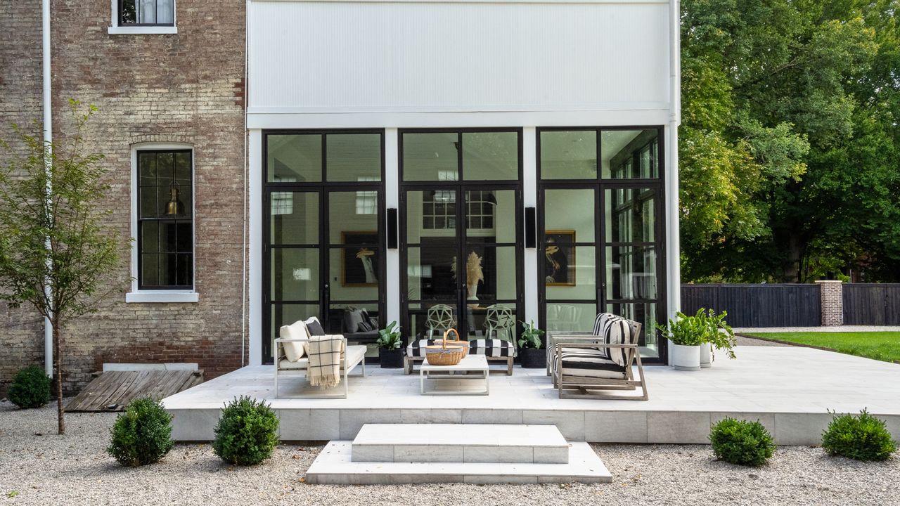 Paved patio outside black framed doors with white and grey sleek sofas and coffee table