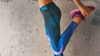 a photo of a woman stretching at the gym wearing bright gym leggings