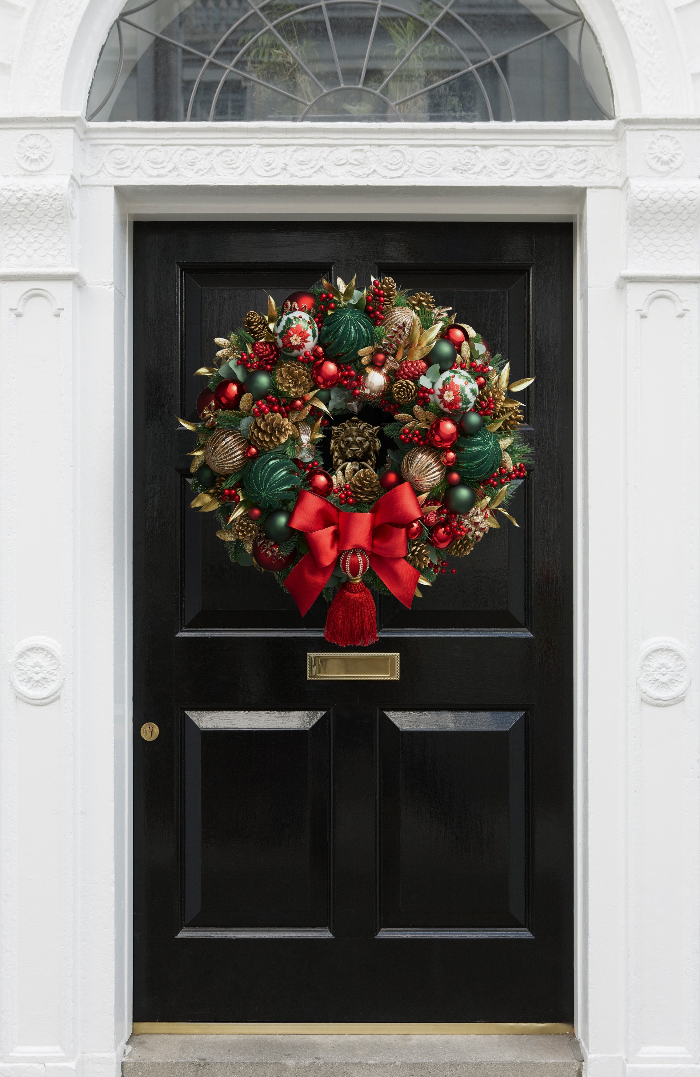 A luxury Christmas wreath hanging on a black front door. The wreath has tassels,bows, jewels, baubles, and golden pine cones on it.