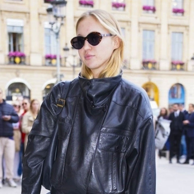Lila Moss wearing a black leather jacket, gray flared pants, and black boots
