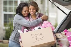 A mother and daughter hug while packing up the car to go to college.