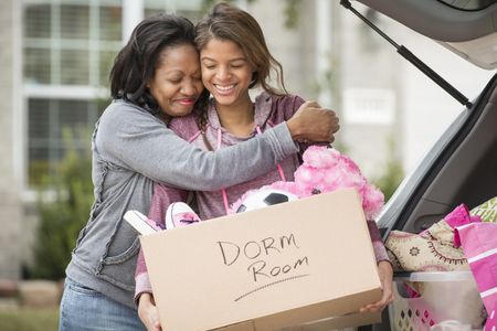 A mother and daughter hug while packing up the car to go to college.