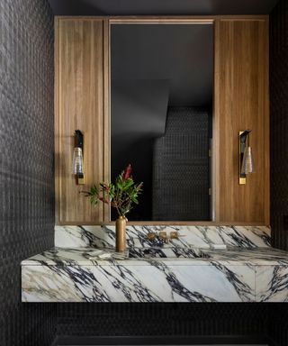 A black wallpapered powder room with a striking marble sink and wood paneling surrounding the rectangular portrait vanity mirror