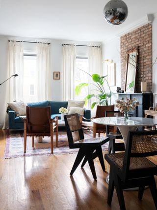 Living-dining space with white painted and exposed brick walls, teal sofa, leather armchairs and small dining table and chair set
