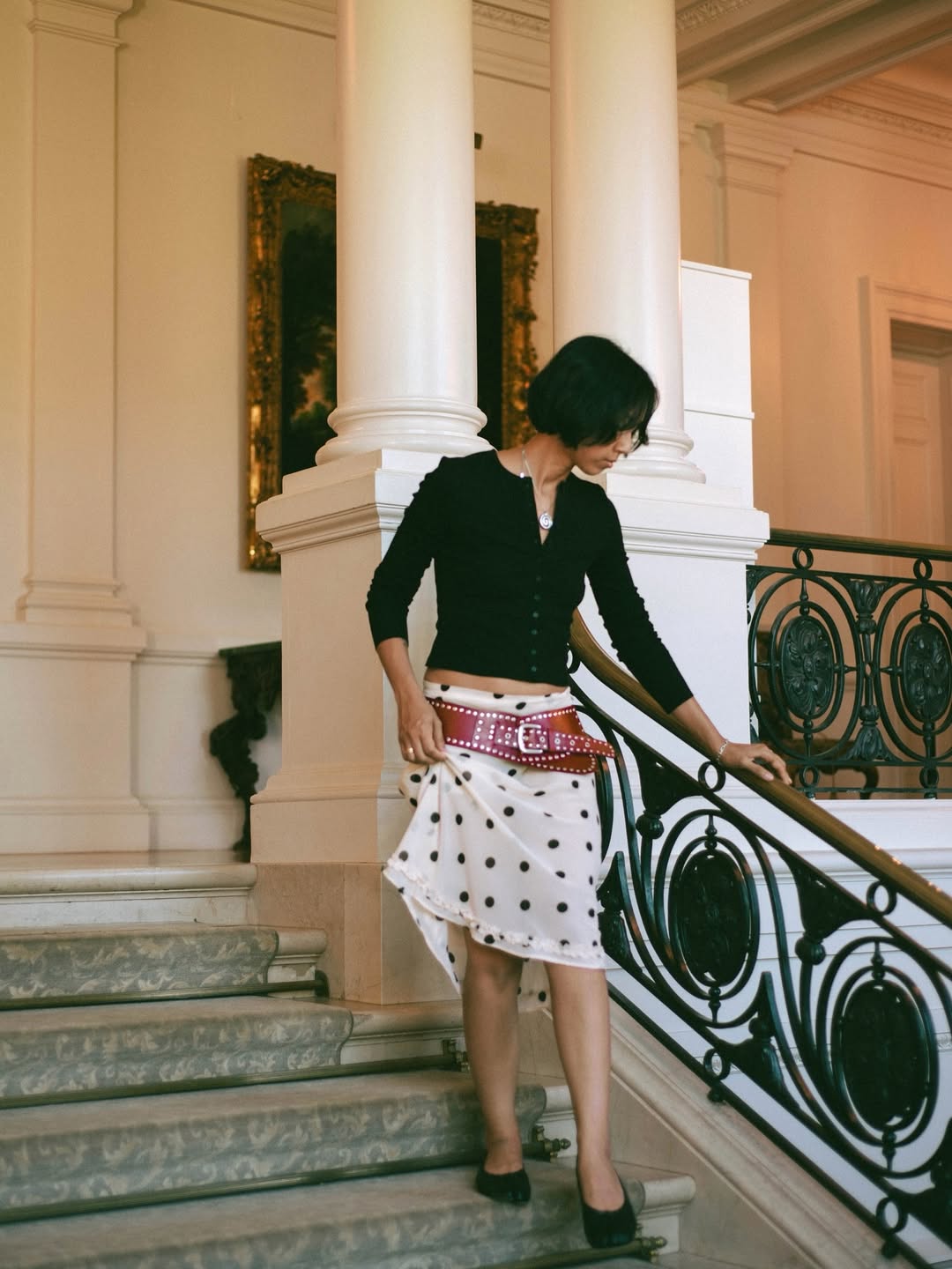 @shhtephs wears a white-and-black polka dot skirt, black long-sleeve top, red belt and black mules