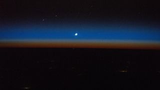 A photograph of Venus as a small dot against the sunset in space