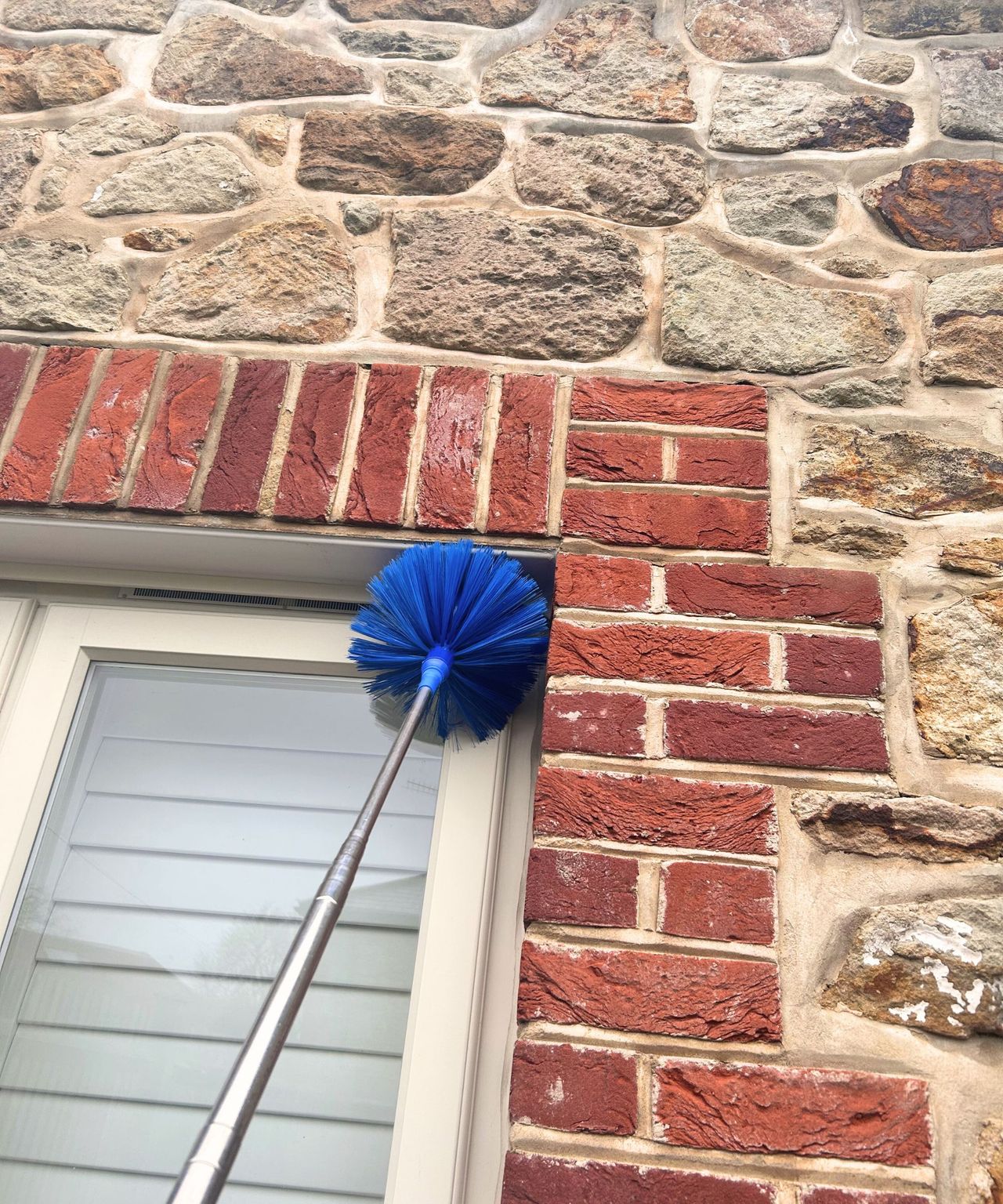Window crevice being dusted with a blue outdoor cobweb duster